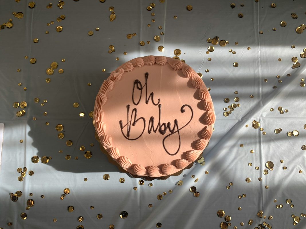 brown cake with 'oh baby' written on the top on a white table with confetti scattered on table top