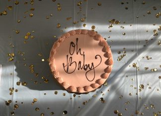 brown cake with 'oh baby' written on the top on a white table with confetti scattered on table top