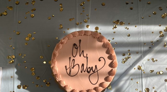 brown cake with 'oh baby' written on the top on a white table with confetti scattered on table top