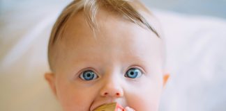 Five Surprising Household Items that Double as Baby Gear colin-maynard via unsplash baby with blonde hair and blue eyes on a white blanket with a block in his mouth