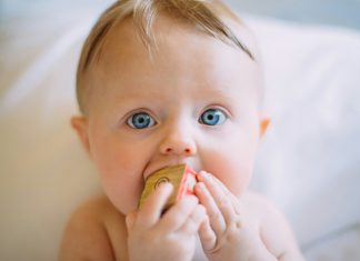 Five Surprising Household Items that Double as Baby Gear colin-maynard via unsplash baby with blonde hair and blue eyes on a white blanket with a block in his mouth