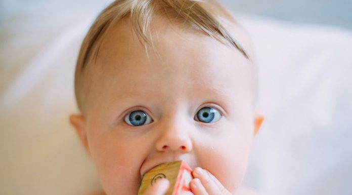Five Surprising Household Items that Double as Baby Gear colin-maynard via unsplash baby with blonde hair and blue eyes on a white blanket with a block in his mouth