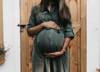 camylla-battani via unsplash pregnant woman in front of a wooden door holding her belly
