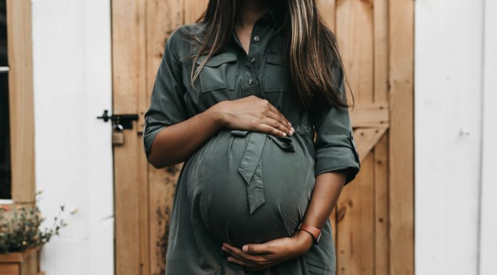 Nine Weeks and Counting… camylla-battani via unsplash pregnant woman in front of a wooden door holding her belly