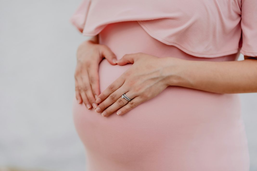 juan-encalada via unsplash pregnant belly in a pink dress with hands on the bump and wedding rings
