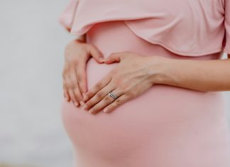 juan-encalada via unsplash pregnant belly in a pink dress with hands on the bump and wedding rings