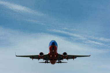 gary-lopater via unsplash red and blue airplane headed for the camera with a cloudy sky behind it
