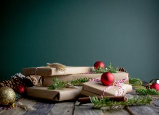 mel-poole via unsplash presents wrapped in brown paper with Christmas tree branches and ornaments around on a dark gray background and a gray wood table