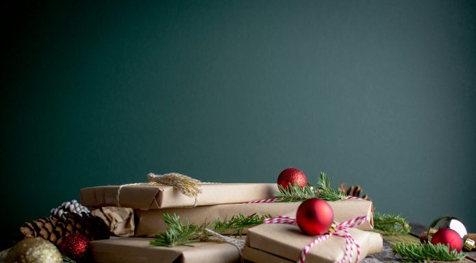 Holiday Photos — Now What? mel-poole via unsplash presents wrapped in brown paper with Christmas tree branches and ornaments around on a dark gray background and a gray wood table