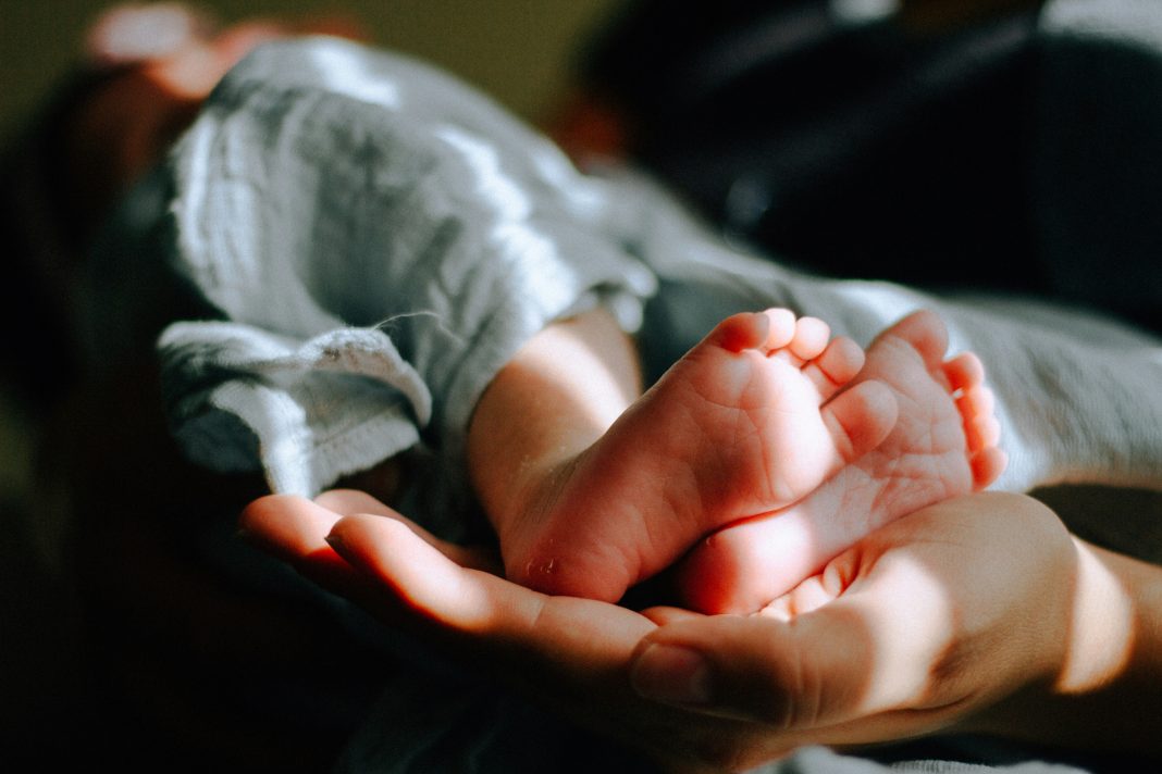omar-lopez via unsplash two baby feet in an adult hand