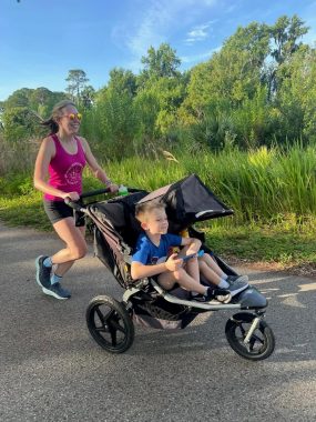 mom smiling while pushing her running stroller with her two kids, smiling. 