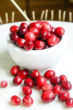 Melissa Di Rocco via Unsplash cranberries in a white bowl and some spilled out on a white countertop