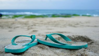 ridwan muhamad iqbal via Unsplash teal flip flops in sand with water behind