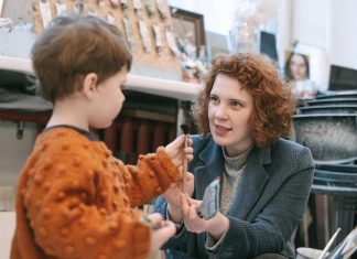 PTA volunteer experience: smiling boy in striped sweater holding a loaf of homemade brown bread at a school bake-sale table.