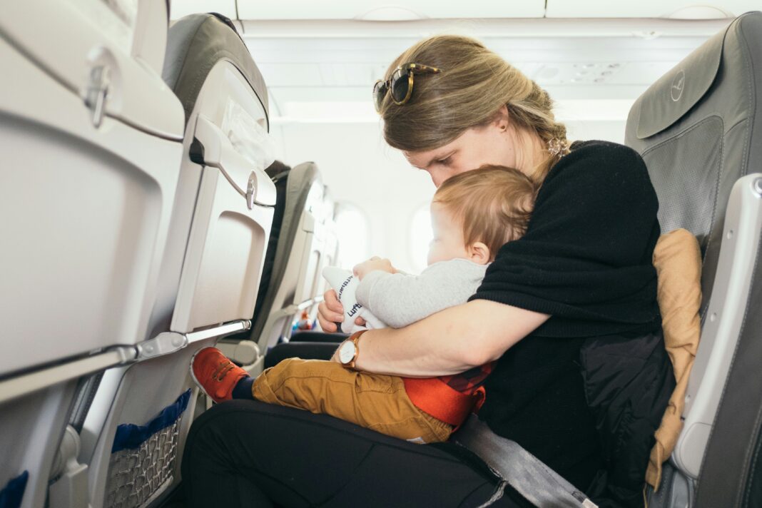 DIY Toddler Travel Help Paul Hanaoka via Unsplash - mom and baby in an airplane seat together looking at something in mom's lap.