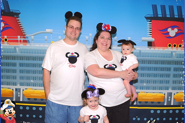 family of four in front of a large picture of a Disney Cruise ship