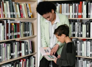 True Life: I’m A PTA Mom PTA mom guiding a young boy through book choices in a bright school library aisle.