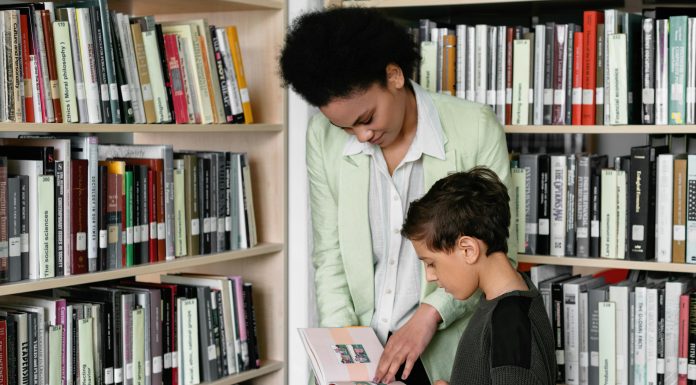 PTA mom guiding a young boy through book choices in a bright school library aisle.