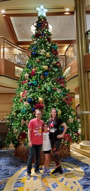 family of three with large christmas tree behind them