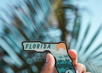 done-by-alex via unsplash a hand holding a sticker in the shape of Florida