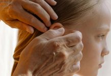 Grandmother gently combs a young girl’s hair in a sun-lit room, attentively inspecting each strand for lice