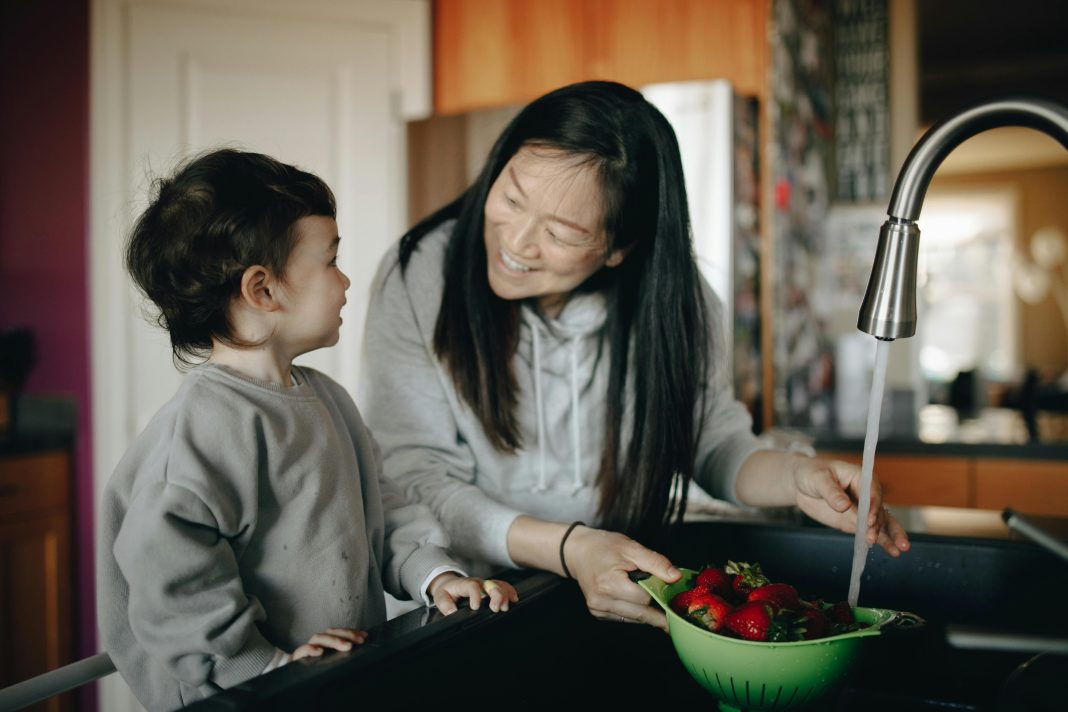 mother smiling at son washng berries for morning school routine
