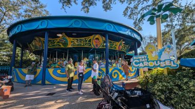 Sunny Day Carousel in blue and yellow with people on the ride and people standing in front of it