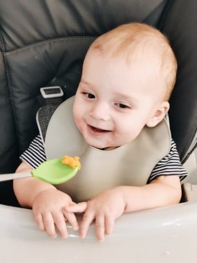 7 month old boy smiling with green baby spoon with sweet potato