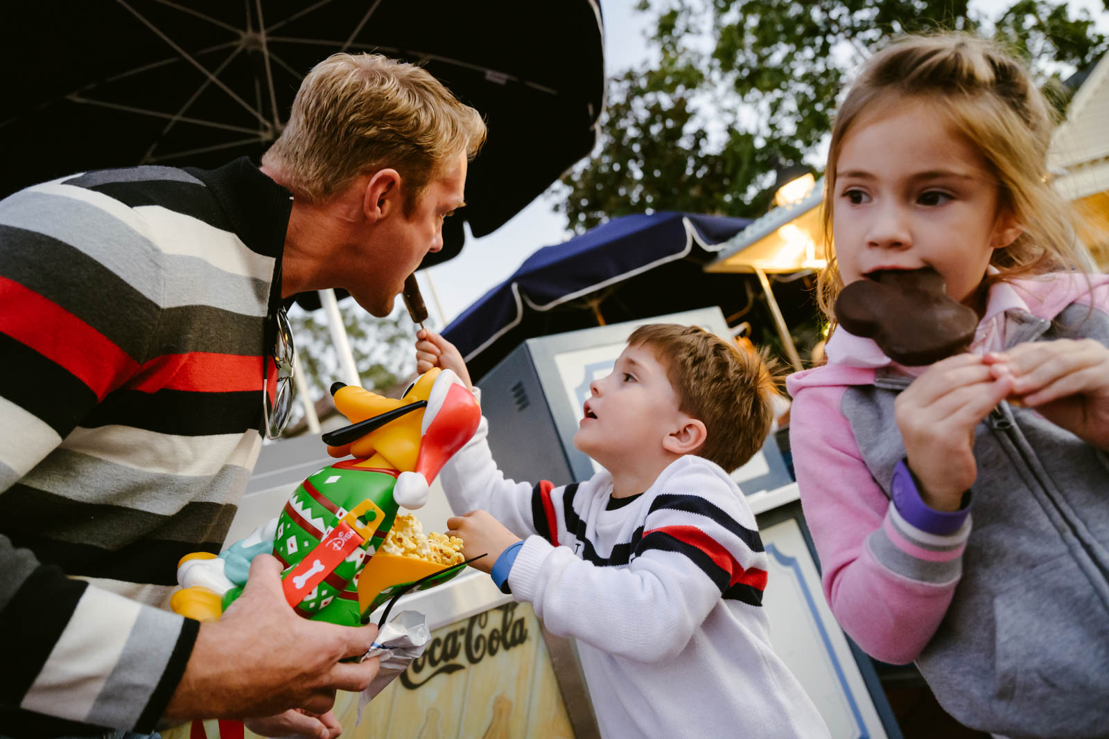 girl eating a mickey shaped ice cream with another kid sharing his with dad