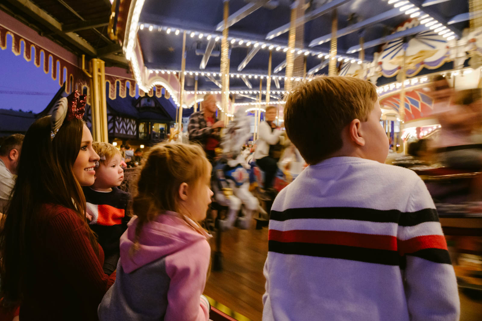 Three kids and mom standing in from tof a moving carousel