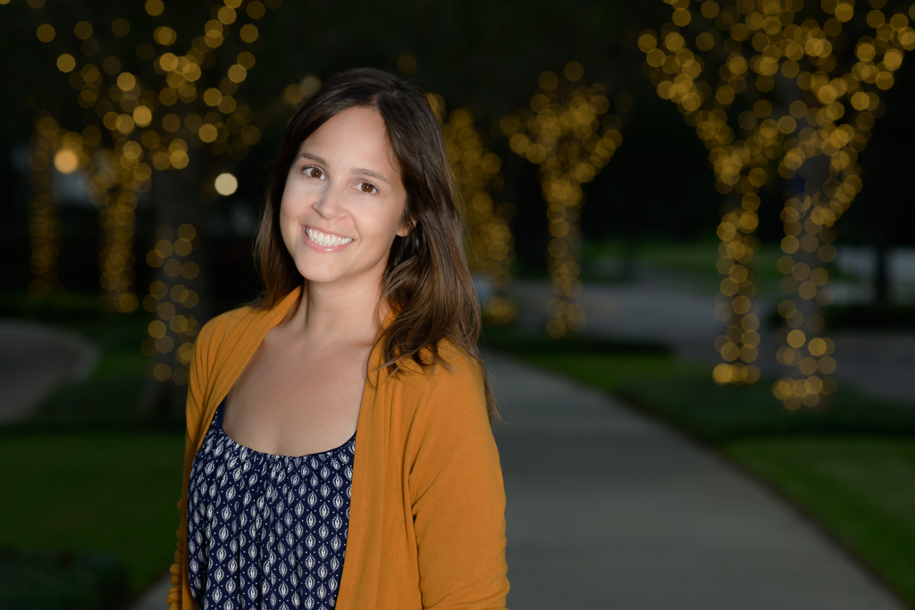 woman on sidewalk with lit up trees behind her