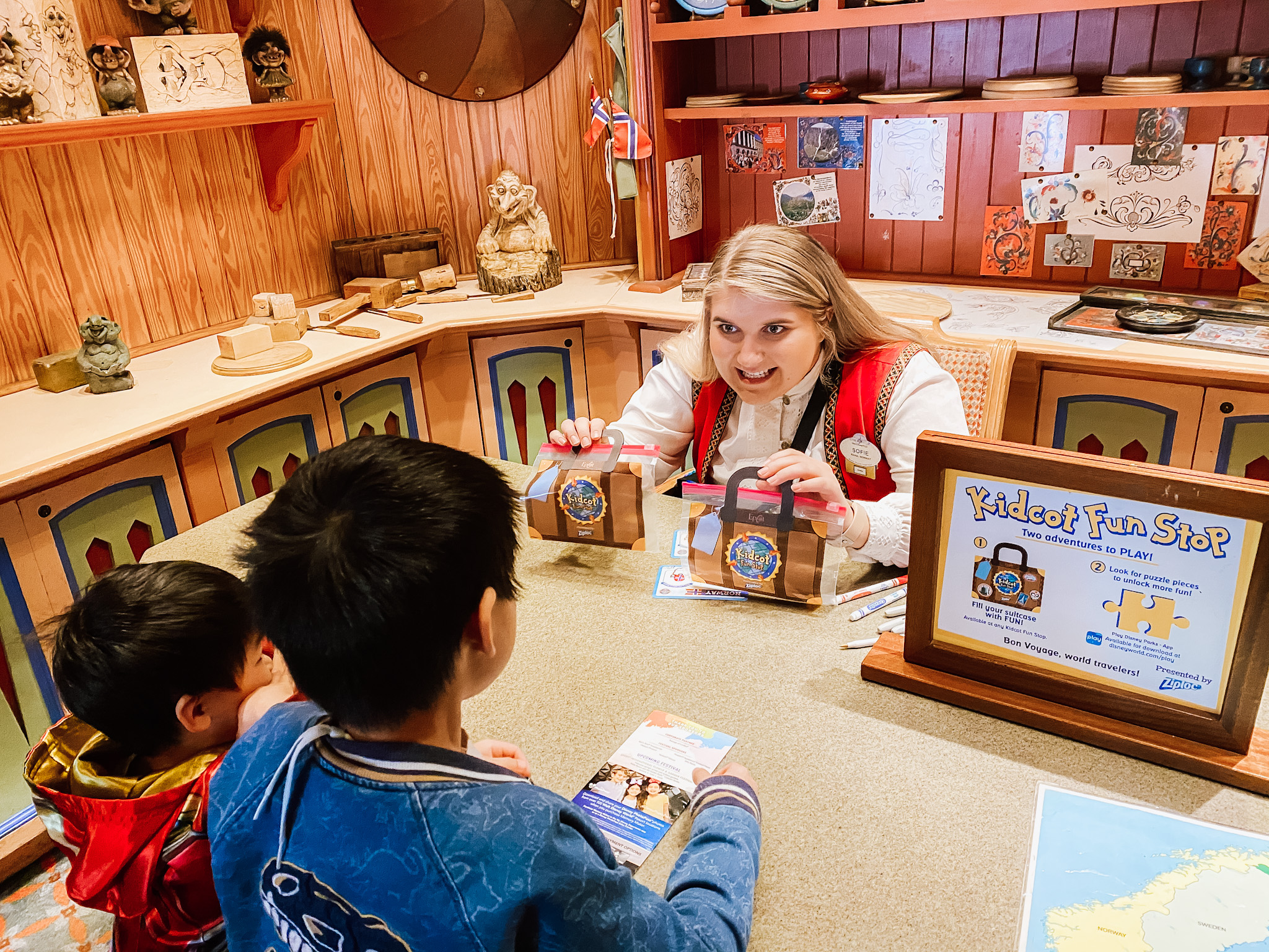 cast member handing two kids their kidcot bags over a table