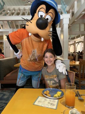 Goofy and girl at a table with fruit and juice on it