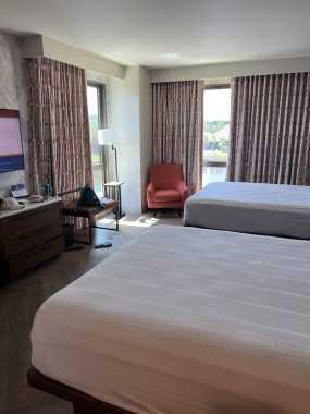 two beds, orange chair and curtains in the corner of a hotel room.