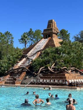 people in a pool with a pyramid shaped water feature behind