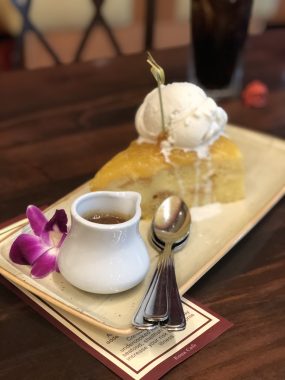 plate with purple flower, cup of caramel color sauce, spoons and cake with ice cream