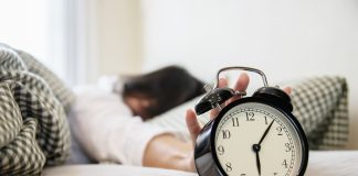 Sleepy woman reaching holding the alarm clock in the morning with late wake up - every day life at home concept; morning better