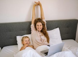 5 Tips to Have Better Mornings! mother stretching in bed smiling while young child is next to her looking at her laptop; morning routine