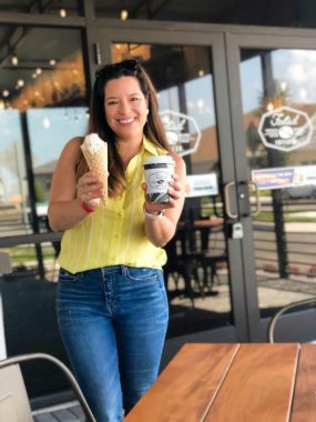 Smiling mom in a yellow blouse and jeans holding two coffees!