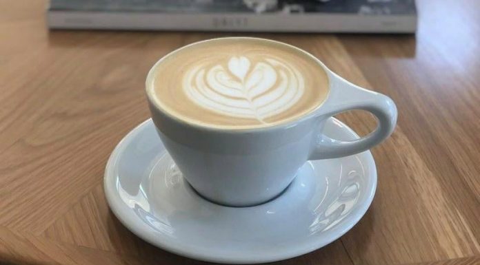 Latte art in a simple white coffee cup and saucer in front of a stack of books on top of a coffee table.