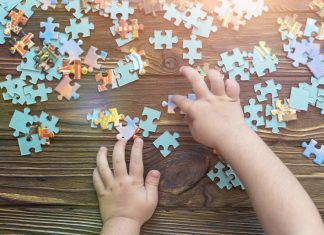 A child's hand collects a puzzle on a wooden background.