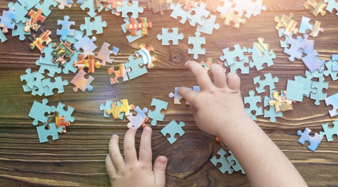 A child's hand collects a puzzle on a wooden background.