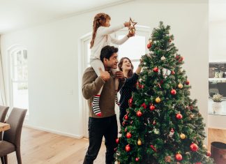 Family decorating a Christmas tree. Young man with his daughter on his shoulders helping her decorate the Christmas tree.