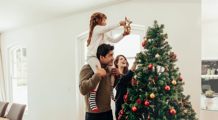 Family decorating a Christmas tree. Young man with his daughter on his shoulders helping her decorate the Christmas tree.