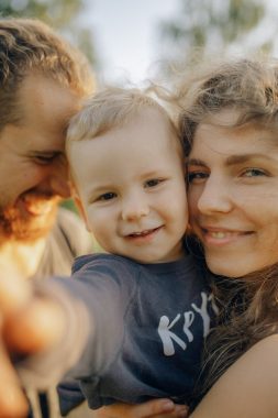 a smiling couple hold their young child in their arms