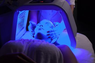 Young woman having LED light facial treatment in beauty salon