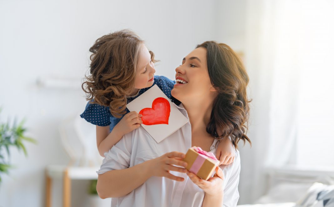 Happy mother's day! Child daughter is congratulating mom and giving her postcard. Mum and girl smiling and hugging. Family holiday and togetherness.