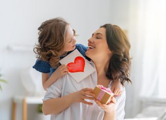 Happy mother's day! Child daughter is congratulating mom and giving her postcard. Mum and girl smiling and hugging. Family holiday and togetherness.