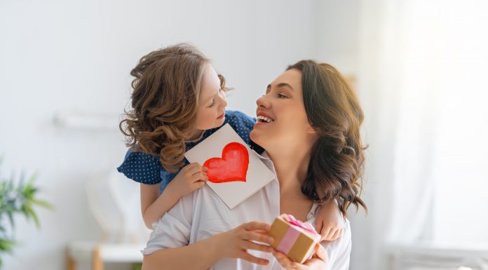 Happy mother's day! Child daughter is congratulating mom and giving her postcard. Mum and girl smiling and hugging. Family holiday and togetherness.