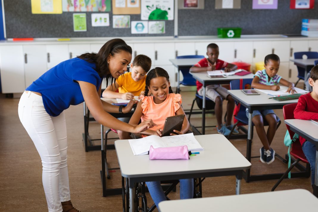 African american female teacher teaching disabled girl to use digital tablet at elementary school. school and education concept